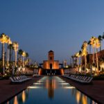 Voyage au Maroc à Marrakech, bassin illuminé bordé de palmiers au crépuscule dans un hôtel de luxe Voyage au Maroc à Marrakech, bassin illuminé bordé de palmiers au crépuscule dans un hôtel de luxe
