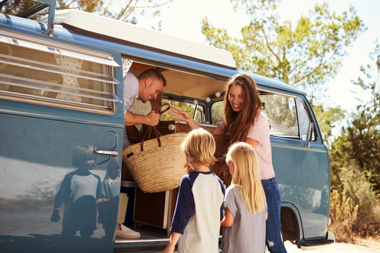 Famille avec deux enfants chargeant un panier dans un van vintage bleu avant un road trip Famille avec deux enfants chargeant un panier dans un van vintage bleu avant un road trip
