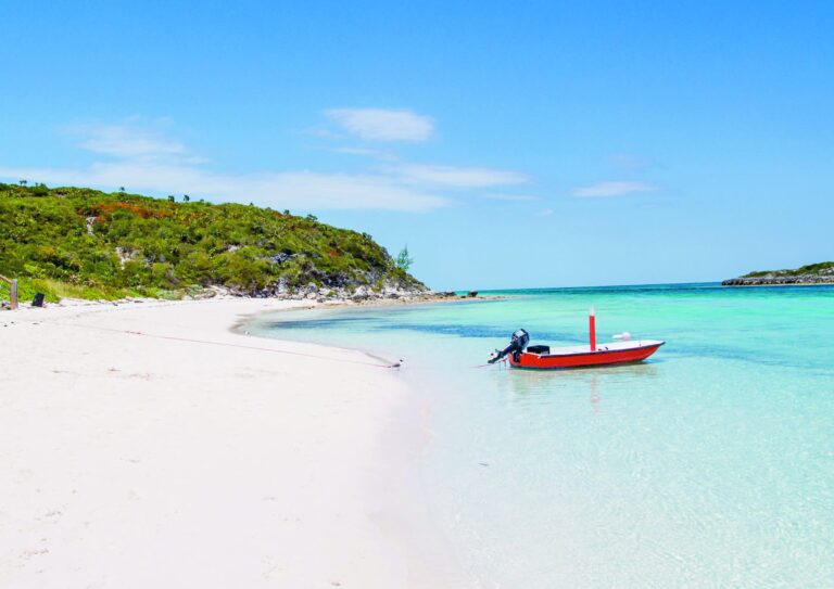 Plage de sable blanc et barque rouge échouée, aux Exuma Cays